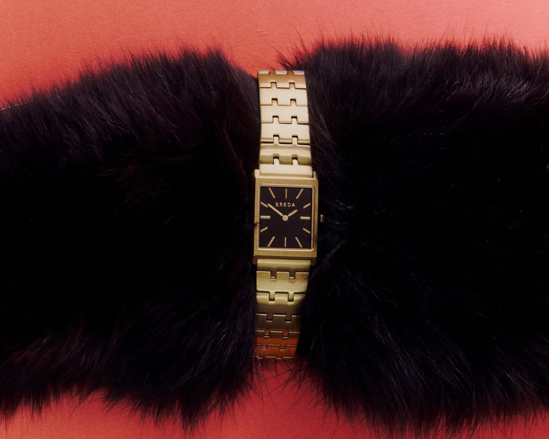 a gold banded and black faced Breda watch over a black faux fur sleeve